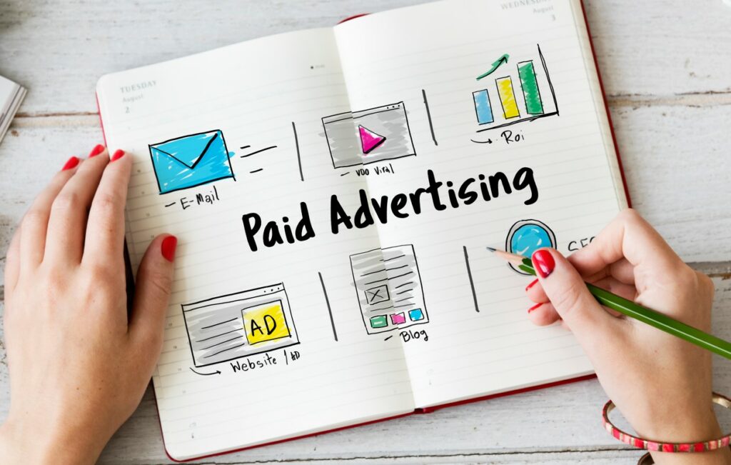 Hands writing in a notebook headed Paid Advertising